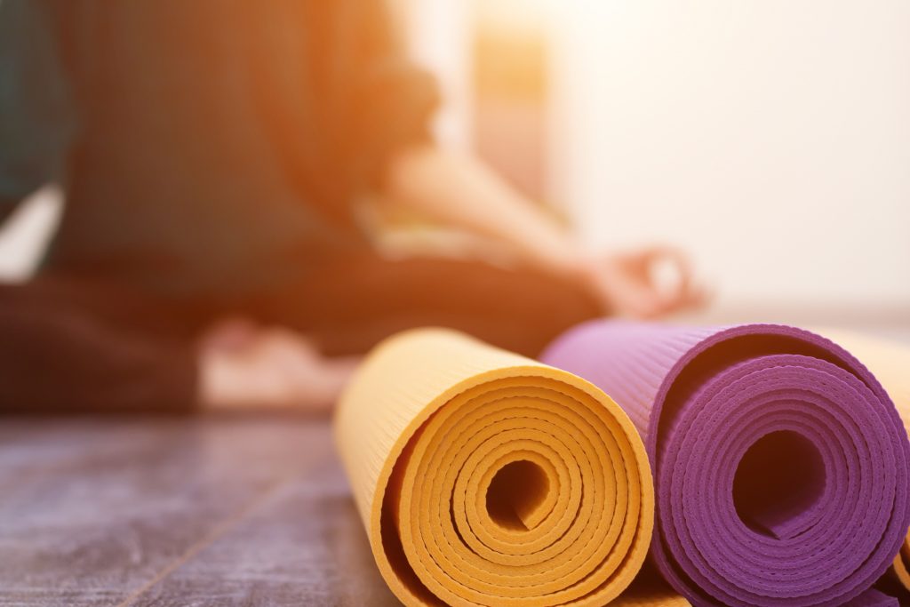 Close up view of two yoga mats with woman behind sitting in yoga pose.