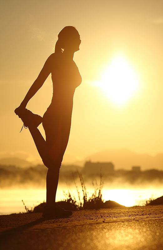 Silhouette of a woman stretching at sunrise with the sun in the background