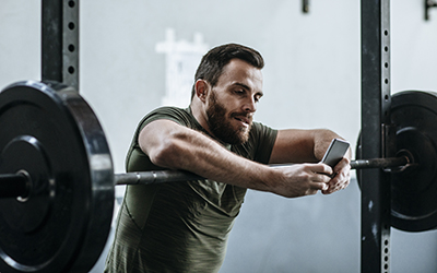 Man reviews video on his phone while resting on squat bar.