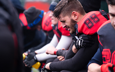 Football player sits on sideline holding arm