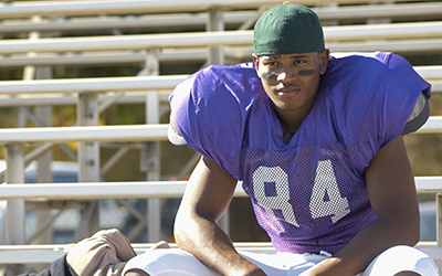 Football player sits in bleachers watching the game unfold.