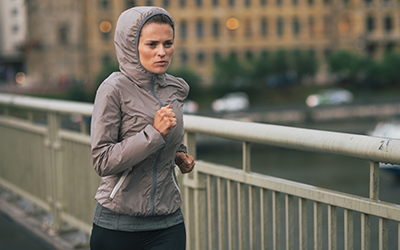 Woman runs across bridge in cold and rainy weather.