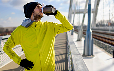 man in yellow coat stops in his outdoor training to take a drink of water.