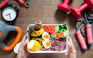 Person holds a pre-workout meal in a white bowl surrounded by exercise accessories.